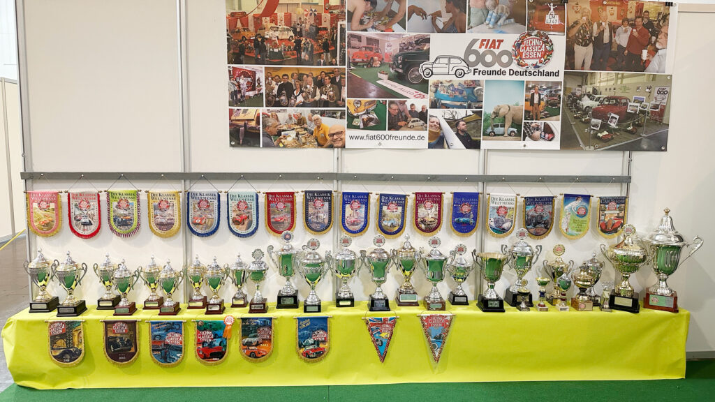 Eine Wand des Messestandes mit den Wimpeln und Pokalen von über 30 Teilnahmen und einem Banner mit Fotos der letzten Jahre.
